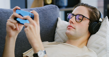 Home, headphones and man with smartphone, video game and streaming service with audio tech....