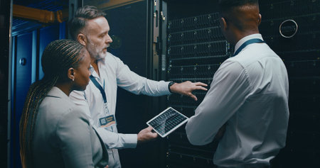 Man, tablet and team with maintenance in server room with cybersecurity, system check or...