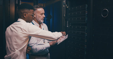 Men, tablet and talk in server room with maintenance, review or report with mentor for system...