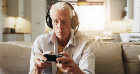 Elderly man, console and playing video games with headphones on sofa for online entertainment....