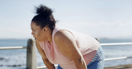 Fitness, woman and tired runner by ocean for health, wellness and workout recovery at promenade....