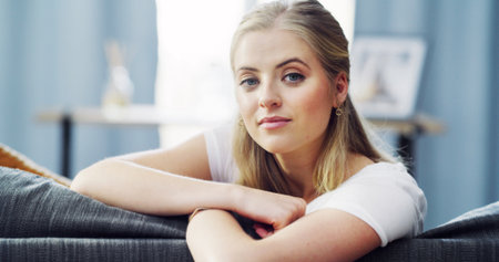 Portrait, house and woman on sofa, relax and weekend break with positivity in living room. Apartment, happiness and person on couch, resting and morning with mindfulness, wellness satisfactionの写真素材