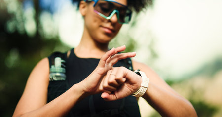 Fitness, running and watch with woman in forest for challenge, performance or progress tracking. Exercise, marathon and time with athlete or runner outdoor in nature for training or workout routineの写真素材