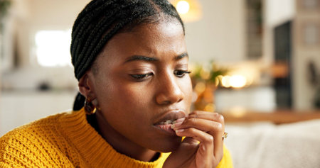 Mental health, biting nails and black woman in home with nerves, overthinking or coping mechanism for study anxiety. Worry, mindset and student in house with bad habit, reflection or trauma in stressの写真素材