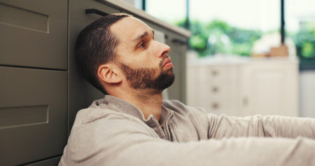 Sad, thinking and man in kitchen with stress, mental health challenge or worry for debt. Depression,...