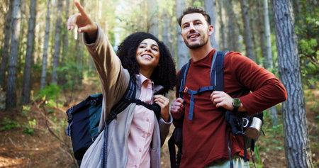 Couple, hiking and point in woods for direction with search, break and happy with backpack for...