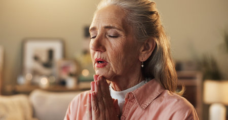 Belief, hope and prayer with senior woman on sofa in living room of home for trust in Christ Jesus....
