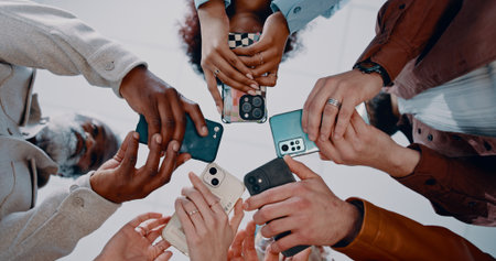 Business people, hands and below with phone in circle for data sync, share or communication in office. Low angle, group or employees with mobile smartphone for networking or connectivity togetherの写真素材