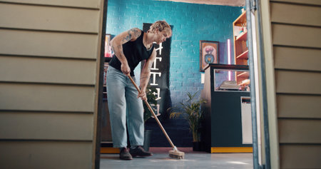 Cleaning, broom and small business with man in tattoo parlor for preparation or start of work. Hygiene, maintenance and sweeping with person in startup studio for chores, responsibility or tasksの写真素材
