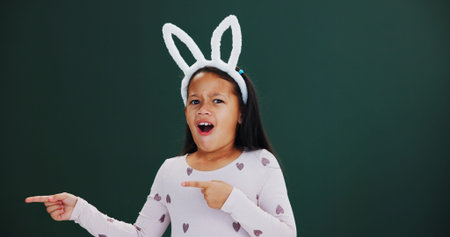 Bunny ears, pointing and portrait with girl child in studio for announcement or notification. Easter...