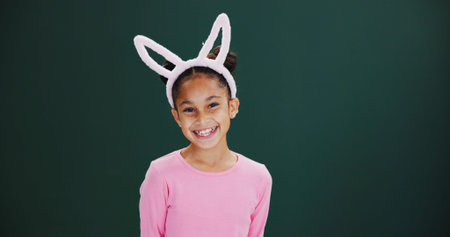 Portrait, bunny ears and girl in studio, smile and happiness on green background. Mockup space, kid...