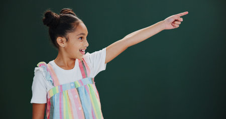 Child, girl and pointing to presentation in studio for news, announcement or mockup. Happy, kid and...