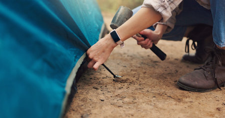 Camping, hands and pitch tent with hammer for weekend shelter, holiday adventure or preparation. Woods, travel and person setting up gear at campsite for outdoor vacation, gear security or survivalの写真素材