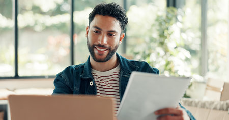 Ecommerce, documents and happy man with laptop in home office for startup, digital marketplace and sales. Entrepreneur, product listing and online order with pc for customer, supply chain or shippingの写真素材