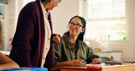 Teenager, student and teacher helping in classroom for education, lesson assistance and explain quiz. Girl, mature woman and learning support of assessment, problem solving tips and homework feedbackの写真素材