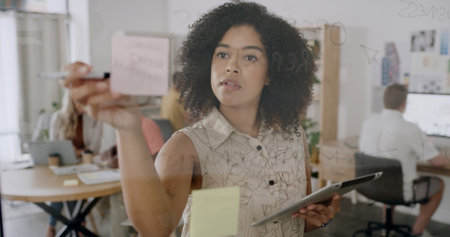 Sticky note, strategy and business woman with tablet, schedule or agenda for consultant. Tech, glass wall and person with creative brainstorming, planning campaign and coworking in officeの写真素材