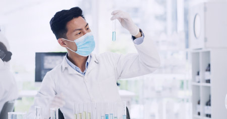 Man, scientist or vial with mask in laboratory for medical research, chemical compound or discovery. Male person, science and checking liquid for scientific experiment, chemistry or study of medicineの写真素材