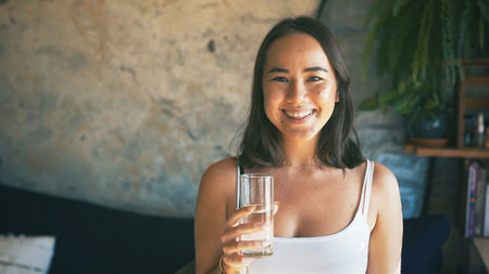 Happy, woman and glass with water in home for liquid hydration, natural nutrients and body detox. Space, person and portrait with fresh beverage in apartment for refreshing drink, thirsty or wellnessの写真素材