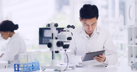 Man, scientist and reading on tablet in lab for research, medical study and experiment results. Person, coworking or microscope with digital, online checklist and healthcare feedback on vaccine trialの写真素材