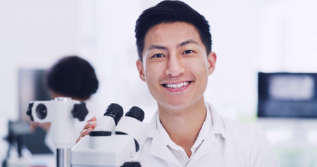 Portrait, scientist and Asian man in laboratory with microscope, medical research and development. Smile, science and face of person with microbiology equipment, professional and career prideの写真素材