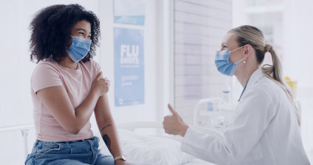 Healthcare, face mask and doctor with woman for thumbs up in hospital for consultation with vaccination. Happy, checkup and medical worker with patient for injection, medicine or medication in clinicの写真素材