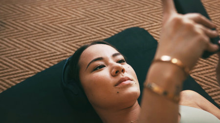 Yoga, headphones and phone with woman on floor for social media, streaming and wellness podcast. Connection, exercise and workout break with above of person in home for fitness, resting and musicの写真素材