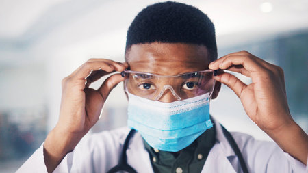 Portrait, black man and doctor with glasses at hospital for eye protection, medical procedure and ppe. Surgeon, safety goggles and face mask to control disease, healthcare risk and hygiene complianceの写真素材