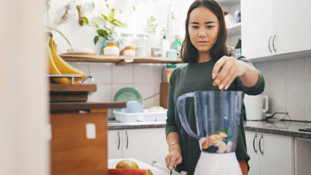 Asian woman, health and fruits in blender for smoothie, detox diet or wellness in kitchen. Mixer, home and person with appliance for vegan ingredients, preparation or nutrition with organic benefitsの写真素材