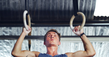 Athlete, man and pull up with gymnastics rings for fitness, exercise and training in low angle. Male person, equipment and intense workout for weightlifting, muscle endurance and power challengeの写真素材