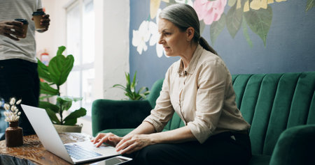 Laptop, woman and mature manager in cafe for product inventory, supplier contact and budget planning. Online review, reputation rating and small business owner with tech and waiter in coffee shopの写真素材