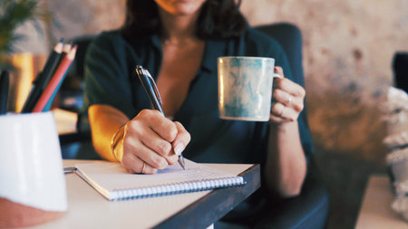Hands, coffee and writing in notebook in home office for meeting schedule, remote work and reminder. Freelancer, personal assistant and tea with notepad for to do list, diary management and planningの写真素材
