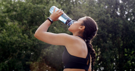 Fitness, woman and water in nature for health, wellness or exercise break with hydration liquid. Bottle, person or thirsty runner with drink outdoor for workout recovery, minerals or sports nutritionの写真素材