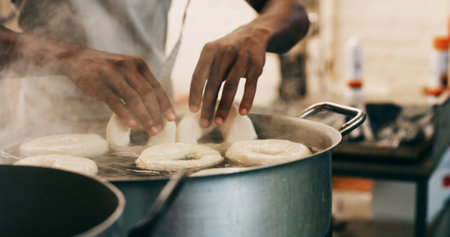 Chef, hands and bagels cooking in water for restaurant food, boiling starch and Polish cuisine. Person, place dough and ingredients in pot for bread roll, meal prep and gluten free recipe in bakery.の写真素材