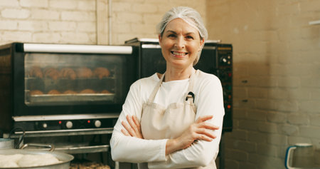 Woman, happy and arms crossed for portrait at bakery, oven and confident with dough for pastry at shop. Person, baker and small business owner with bread, smile or kitchen at store in Germanyの写真素材