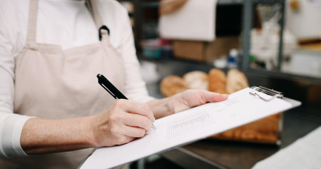 Baker, hands and writing on document in kitchen for supplies, stock or order. Pastry chef, clipboard and woman in bakery for inventory notes, checklist and schedule with signature in businessの写真素材