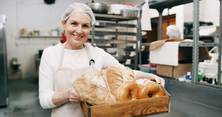 Woman, bakery and happy with bread basket in portrait, pride and entrepreneur with product at store. Mature person, smile and small business owner in kitchen for pastry, buns and bagels in Germanyの写真素材
