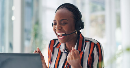Video call, fist pump and black woman with laptop for achievement, success and kpi target. African person, consultation and excited in workplace with headset, celebration and customer service goalsの写真素材