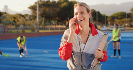 Coach, hockey and happy woman with phone call for match organization, conversation and event info. Planning, mobile or sport trainer with clipboard on turf, game arrangement and local league opponentの写真素材