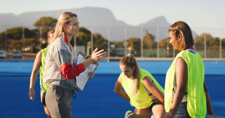 Women, coach and hockey team with clipboard, game planning and feedback for training at club. People, group and athlete with checklist, discussion or insight for fitness routine at sports groundの写真素材