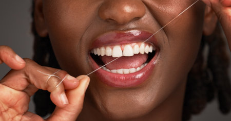 Woman, teeth and hygiene with dental floss in studio for cleaning on a gray background. Closeup, female person or mouth of model with smile, wire or thread for tooth cavity, gum care or oral healthの写真素材