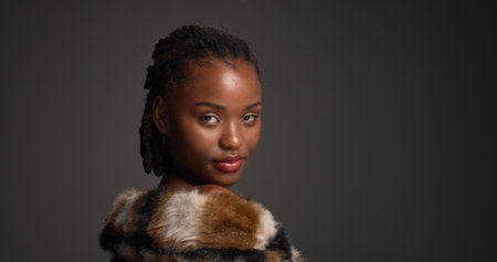 Beauty, fur coat and portrait with black woman on studio space for cosmetics or dermatology. Aesthetic, confident and fashion with serious African model isolated on gray background for skincareの写真素材