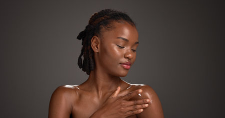 Beauty, skincare or black woman with lotion in studio, hydration or wellness benefits in apply. Shine, dermatology or person with moisturizing glow cream, body care or mockup space on gray backgroundの写真素材