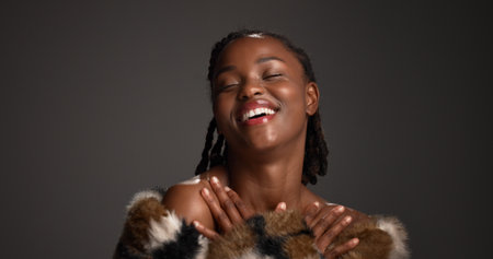 Pride, black woman and makeup for beauty in studio with cosmetics, facial glow and aesthetic. Space, female person and happiness for luxury shine, fur coat and glamour for makeover on gray backgroundの写真素材