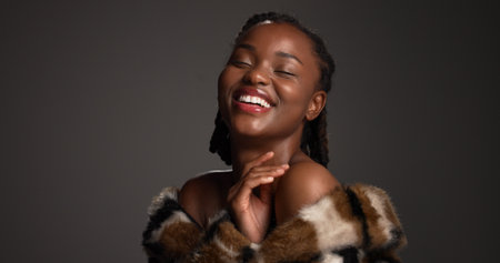 Smile, black woman and laughing for beauty in studio with cosmetics, facial glow and aesthetic. Space, female person and makeup for luxury shine, fur coat and glamour for makeover on gray backgroundの写真素材