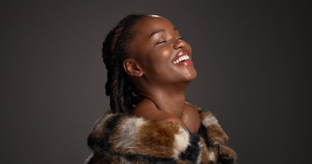 Smile, black woman and makeup for beauty in studio with cosmetics, facial glow and aesthetic. Space, female person and confidence of luxury shine, fur coat and glamour for makeover on gray backgroundの写真素材