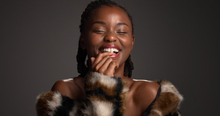 Happy, black woman and confident for beauty in studio with cosmetics, facial glow and aesthetic. Space, female person and makeup for luxury shine, fur coat and glamour for makeover on gray backgroundの写真素材