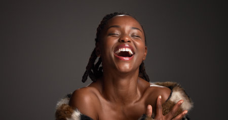 Happy, black woman and laughing for beauty in studio with cosmetics, facial glow and aesthetic. Space, female person and makeup for luxury shine, fur coat and glamour for makeover on gray backgroundの写真素材