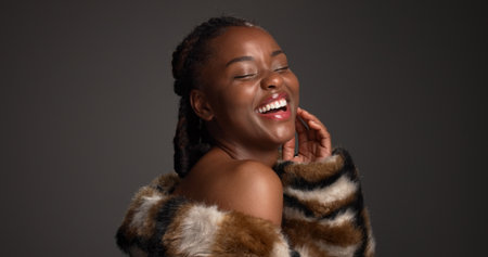 Luxury skincare, beauty and black woman laugh in studio with glow, self care and glamour. Makeup, cosmetics and model with fur coat for aesthetic, healthy skin and funny on dark background spaceの写真素材