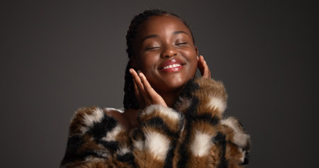 Luxury makeup, beauty and black woman in studio with self care, glow or glamour with cosmetology. Smile, cosmetics and model with fur coat for aesthetic, makeover and touch face on dark backgroundの写真素材
