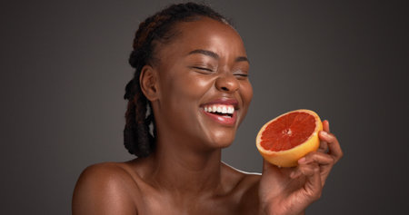 Laugh, grapefruit and black woman with skincare in studio with natural, health or organic glow. Vitamin c, happy and African person with citrus fruit for dermatology hydration by gray background.の写真素材